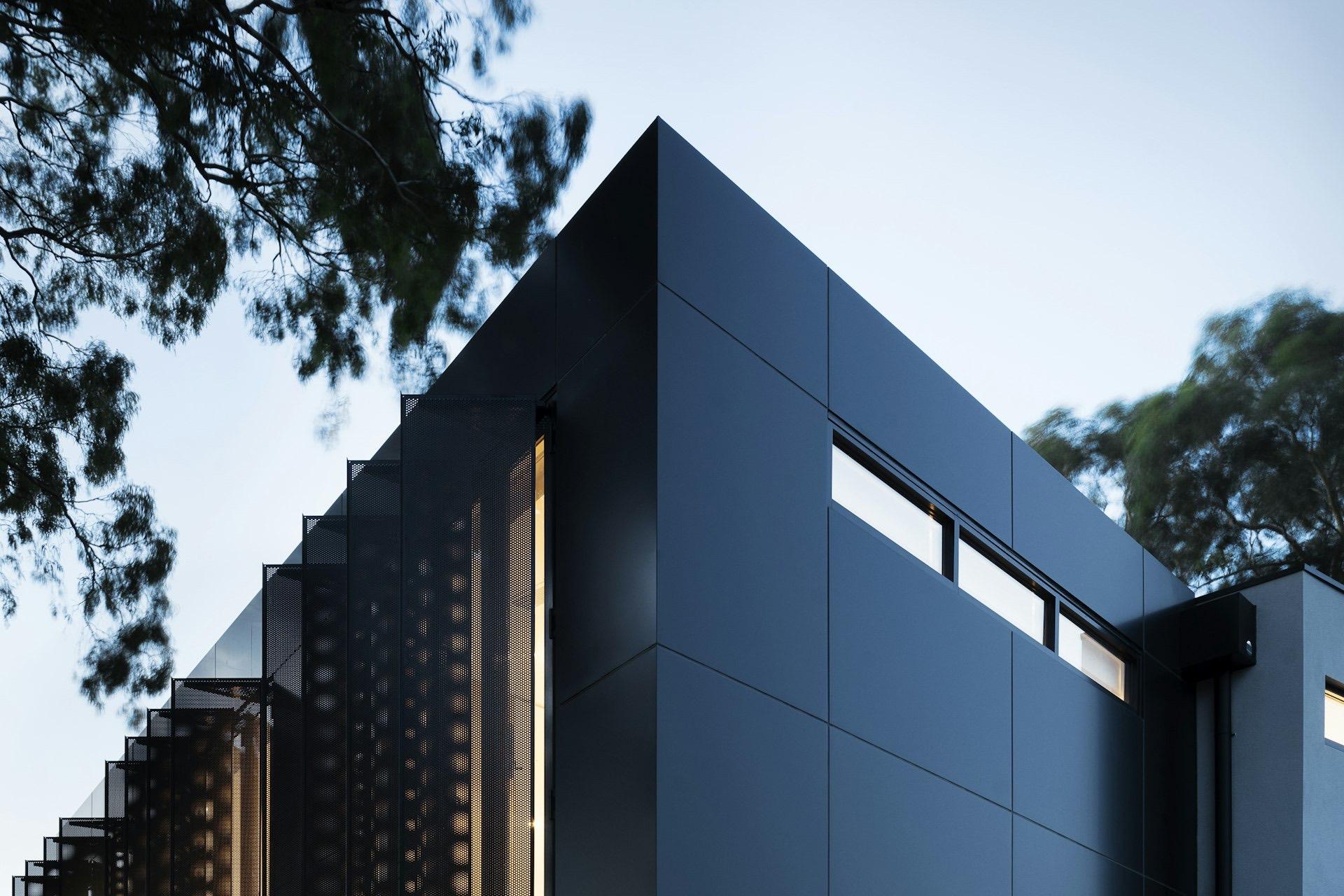 A modern dark-clad luxury residence at dusk with warm glowing timber screens